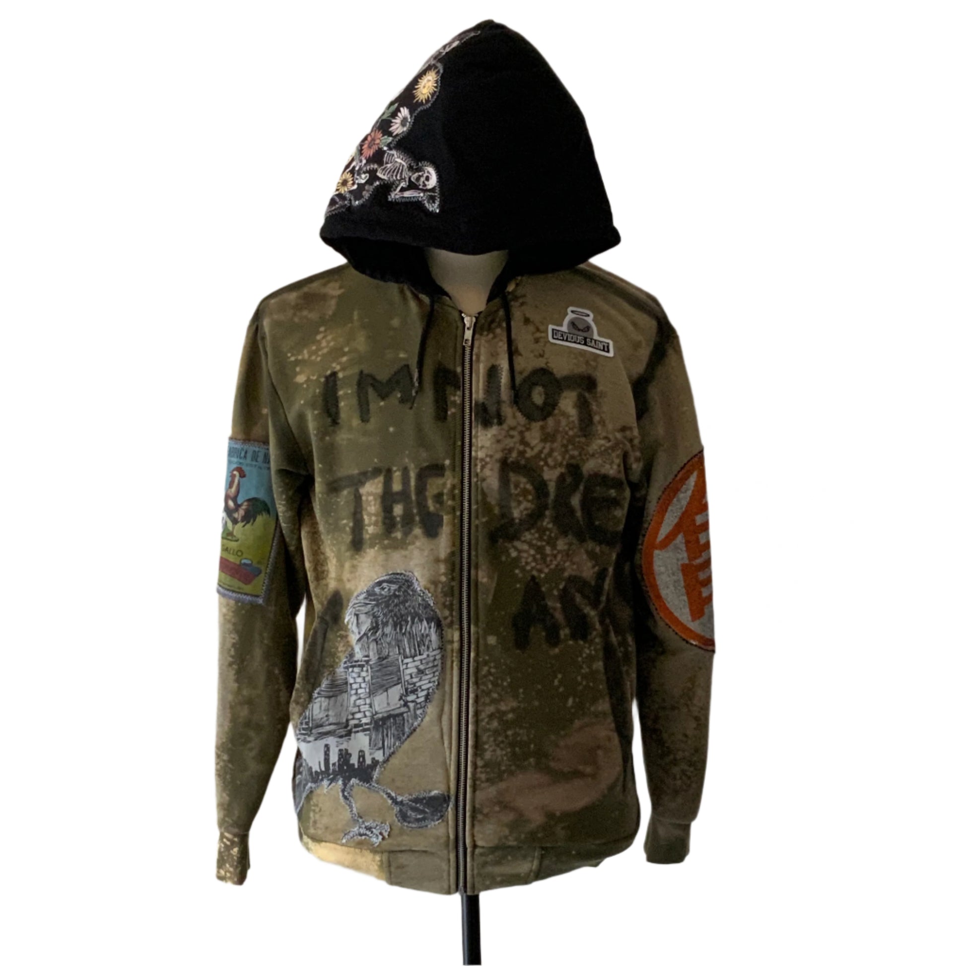 I’M NOT THE DREAM hoodie: Olive camo, black hood with floral and skeleton design, eagle-cityscape embroidery, rooster patch, DEVIOUS SAINT tab, bold streetwear-military style.