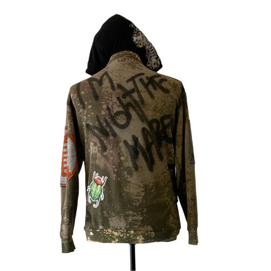 Custom army-green hoodie with bleach distressing, spray-painted I'M NOT THE MARE, colorful patches, and graffiti design. Represents bold, unique style from DEVIOUS SAINT.