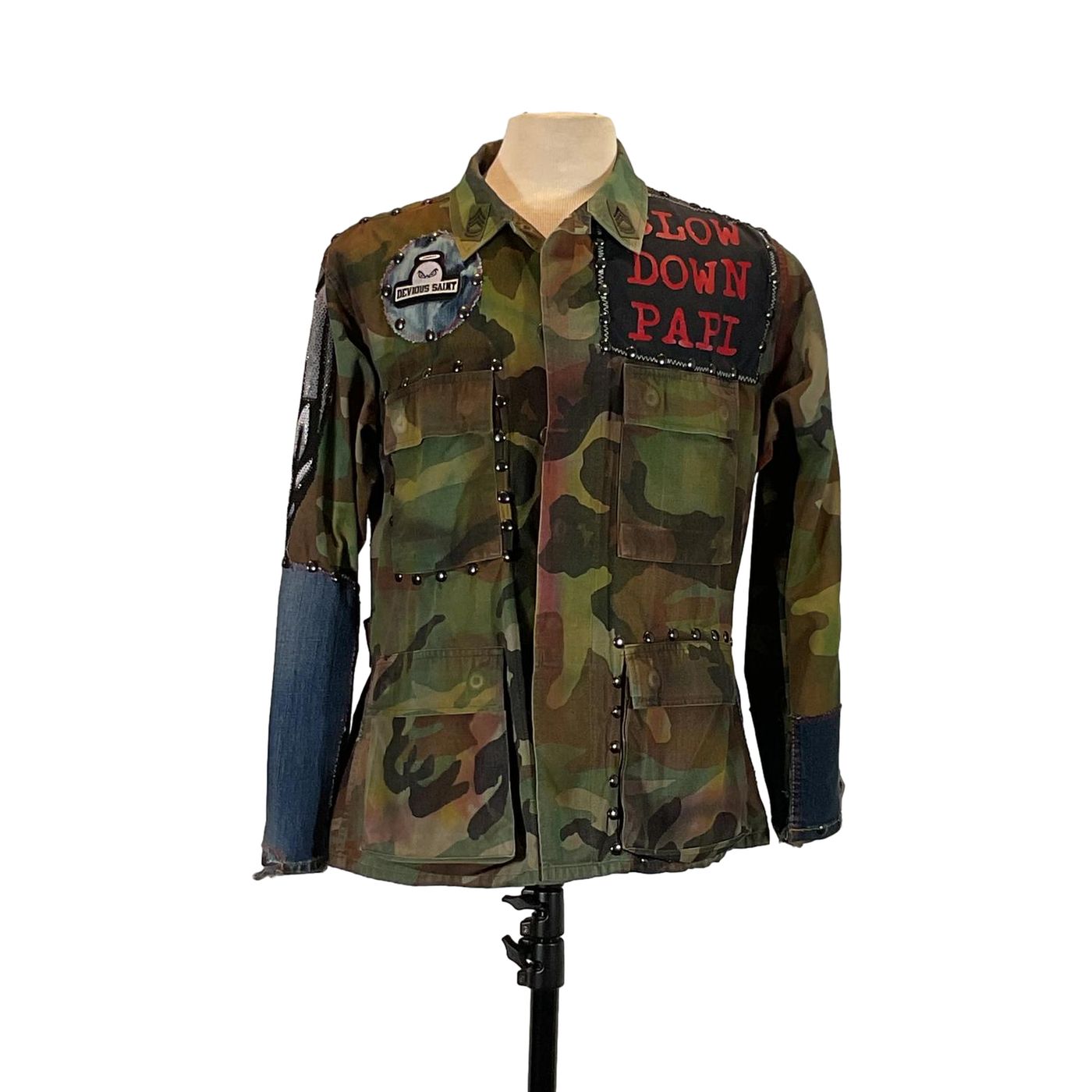 BUITRES Men's Custom Jacket by Devious Saint, featuring camouflage design with patches and rhinestones, displayed on a mannequin, combines unique style and bold artistry.