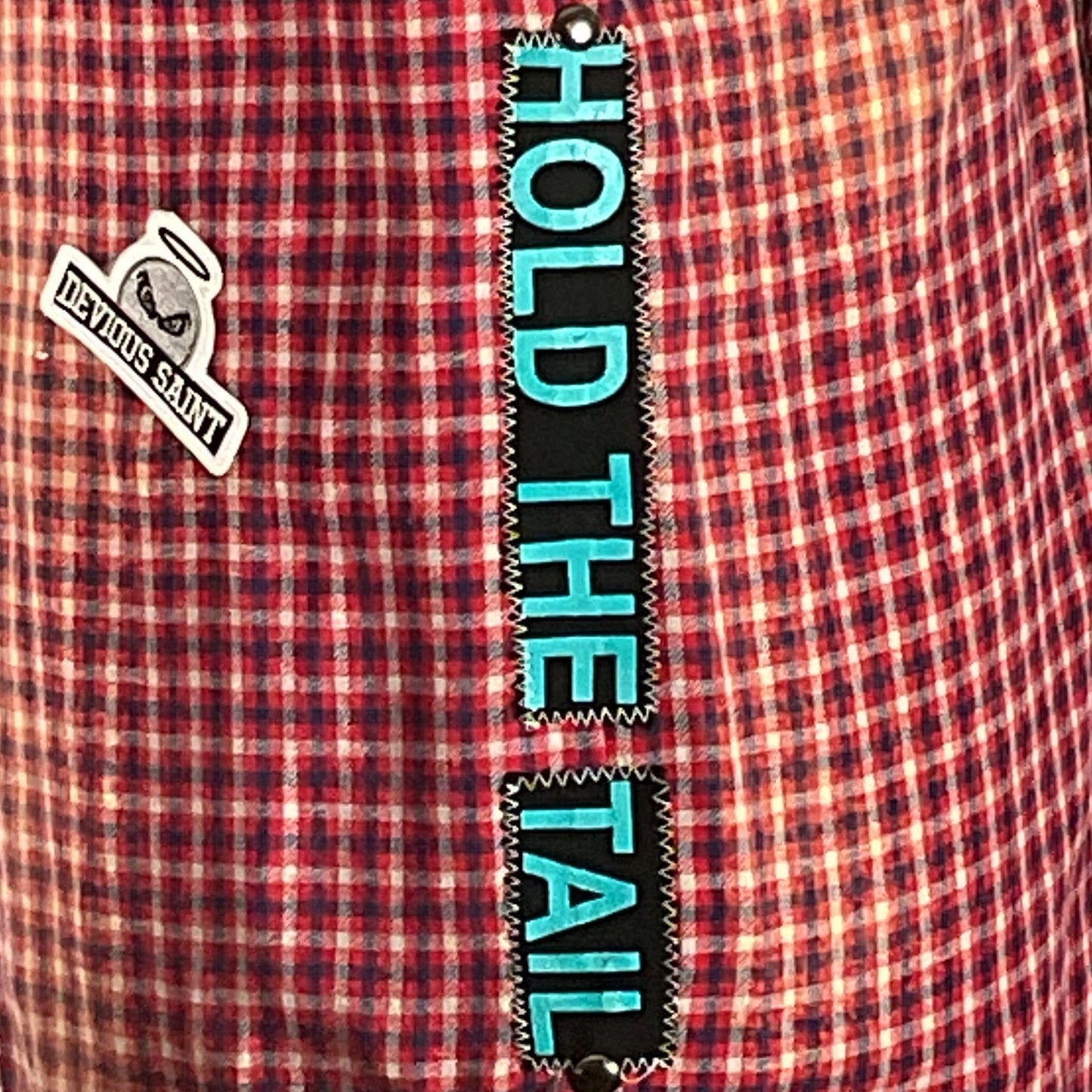 Close-up of a unique, hand-patched flannel shirt with metal studding, embodying sustainable fashion. Features I NEED A COCKTAIL design, showcasing the bold style of DEVIOUS SAINT.