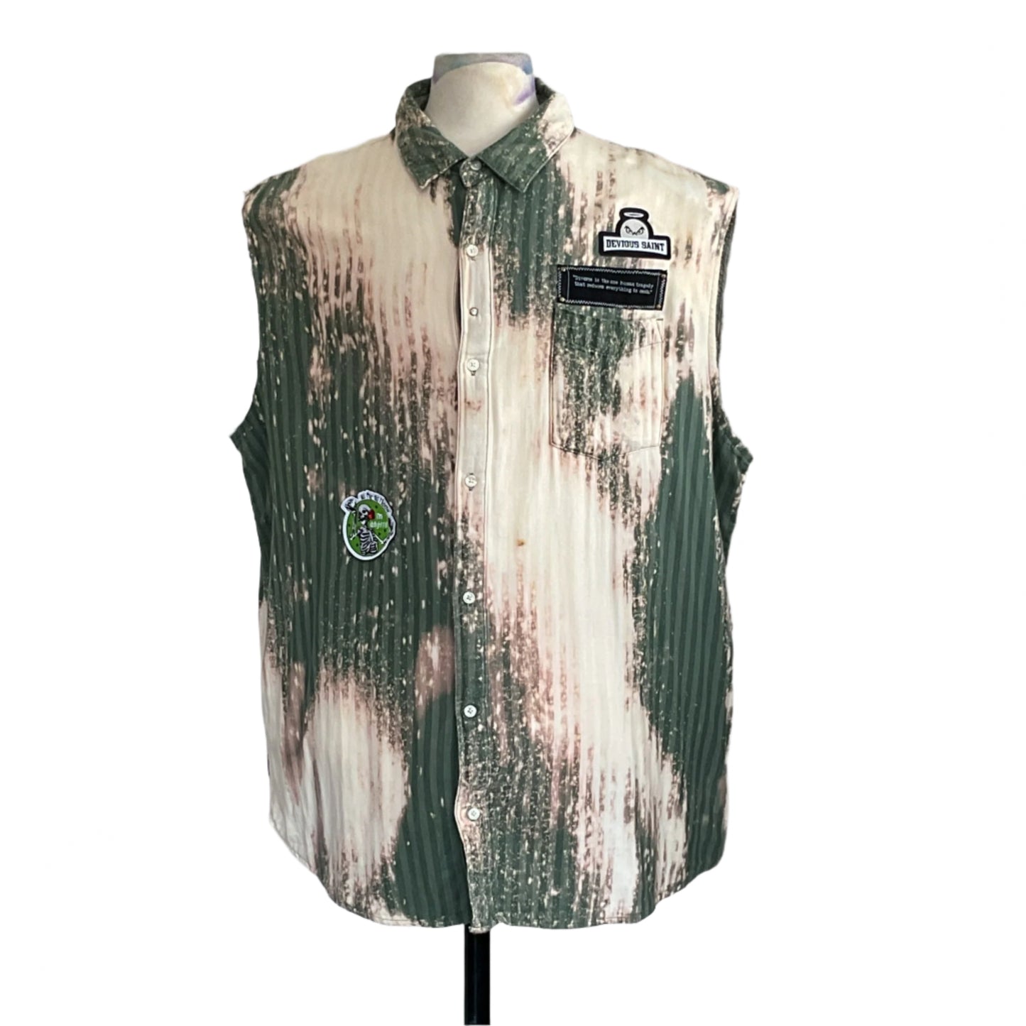 PATCHWORK BEAR sleeveless shirt on mannequin, green-and-white pin-striped with bleached patches, DEVIOUS SAINT patch, cartoon skeleton patch, evokes rugged, warrior spirit.
