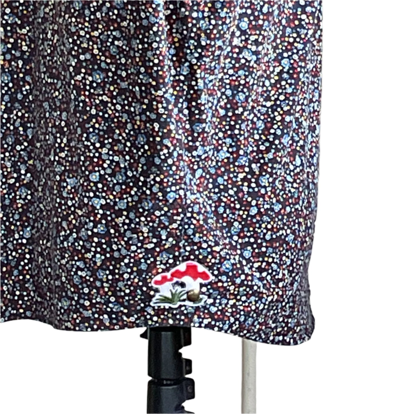 Lower portion of a dark garment with a tiny floral print and an embroidered mushroom patch, showcasing Devious Saint's unique, artistic style.