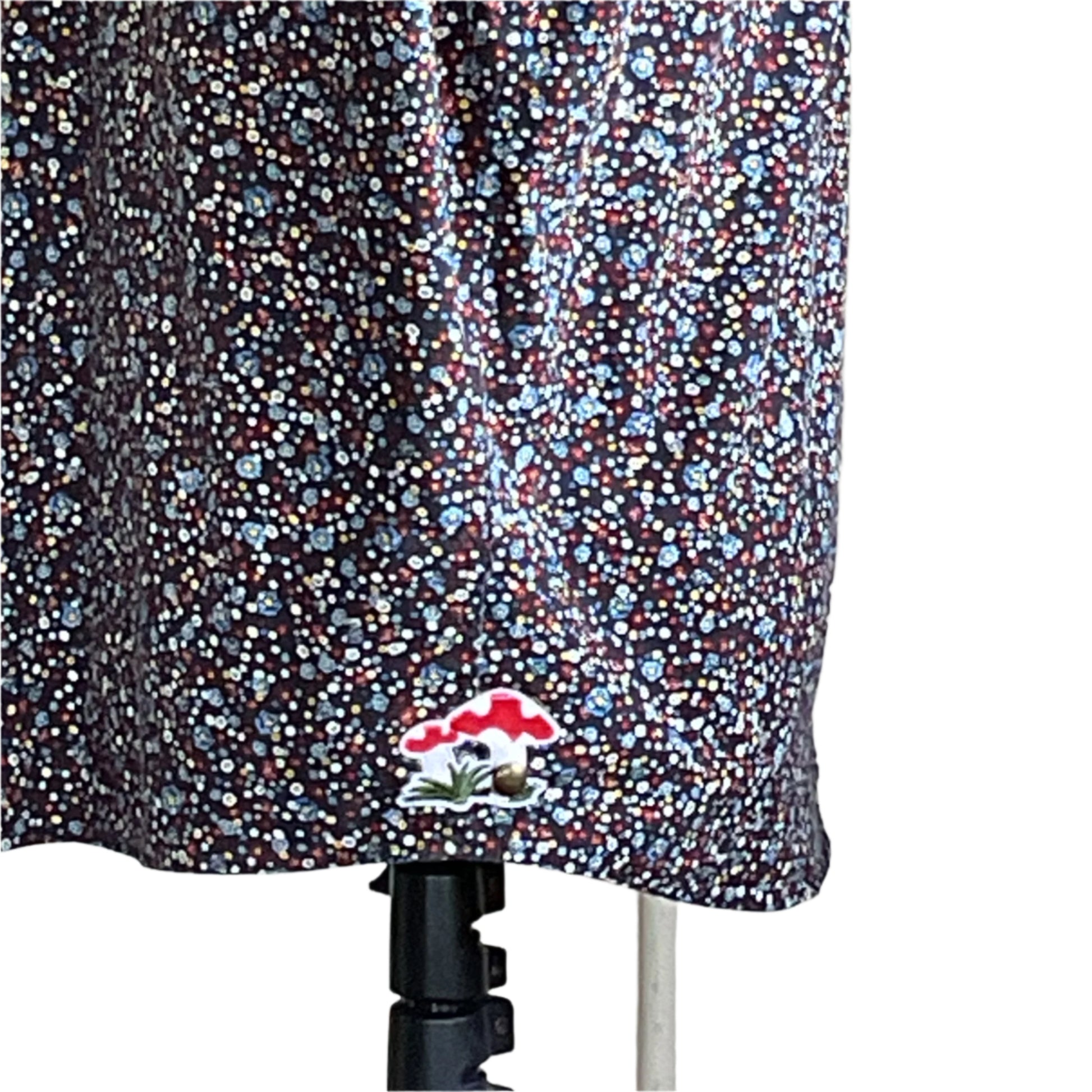 Lower portion of a dark garment with a tiny floral print and an embroidered mushroom patch, showcasing Devious Saint's unique, artistic style.