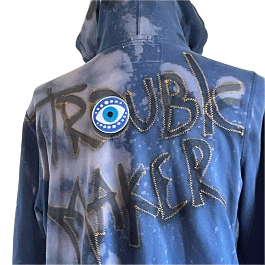 TROUBLE MAKER | eCustom Men's Hoodie featuring a zig-zag gold-stitched phrase with an evil-eye patch, showcasing Devious Saint's rebellious, distinctive style.