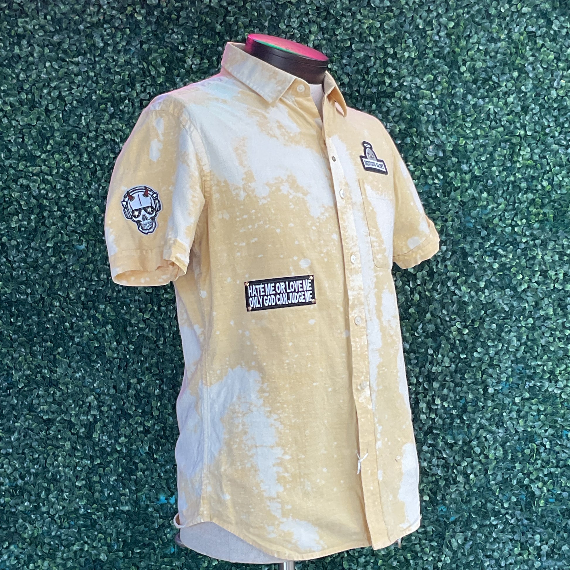 Yellow cotton shirt with mottled pattern, featuring a kettlebell logo, HATE ME OR LOVE ME patch, and skull with headphones patch, displayed on mannequin.
