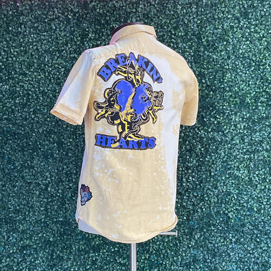 Yellow cotton button-up shirt featuring a large blue heart graphic with cherubs and BREAKIN’ HEARTS text, displayed on a mannequin, capturing bold, distinctive style.