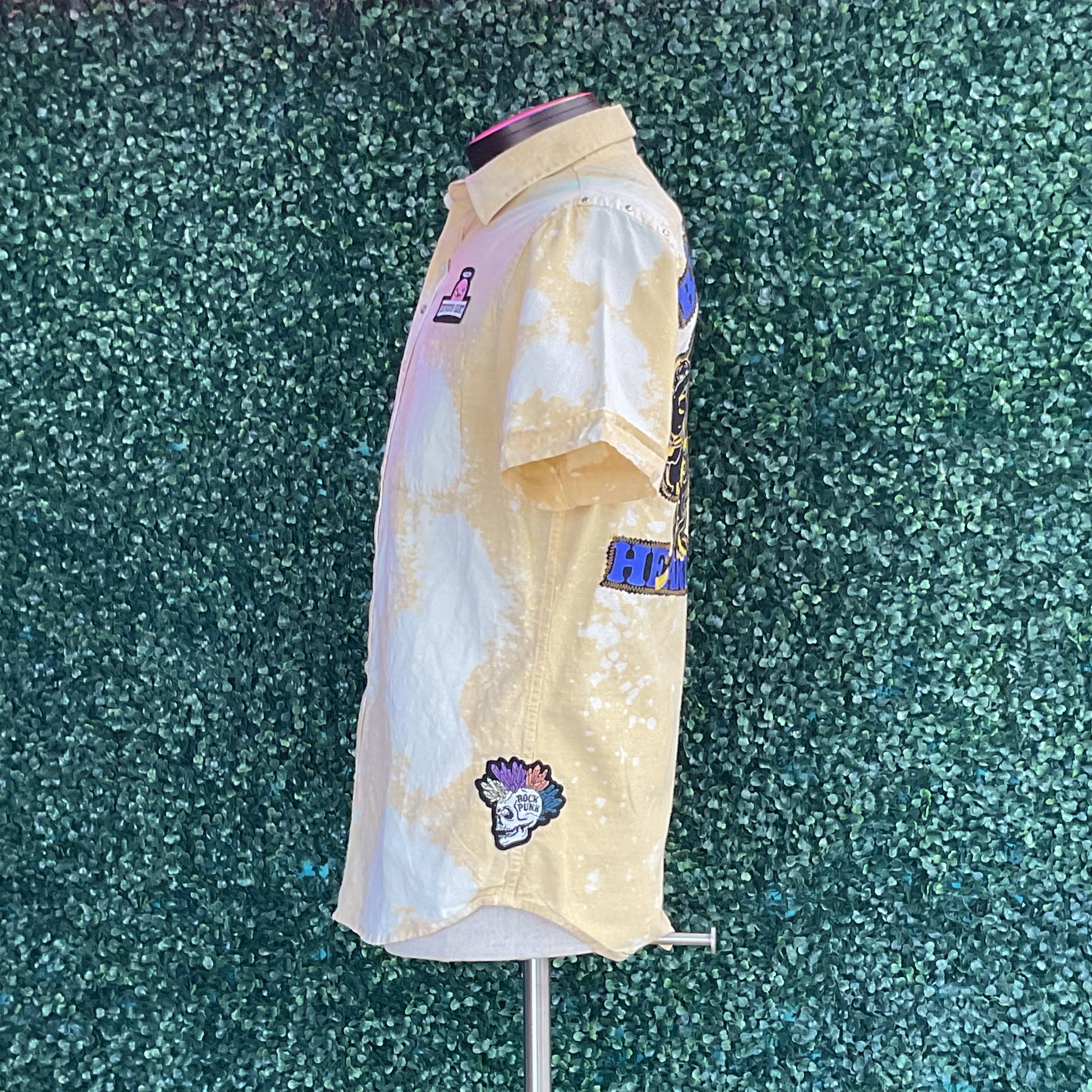 Mannequin wearing Yellow Cotton shirt, featuring acid-washed pattern and patches like a skull with flowers, ROCK PUNK text, and chest emblem, showcasing DEVIOUS SAINT's distinctive style.